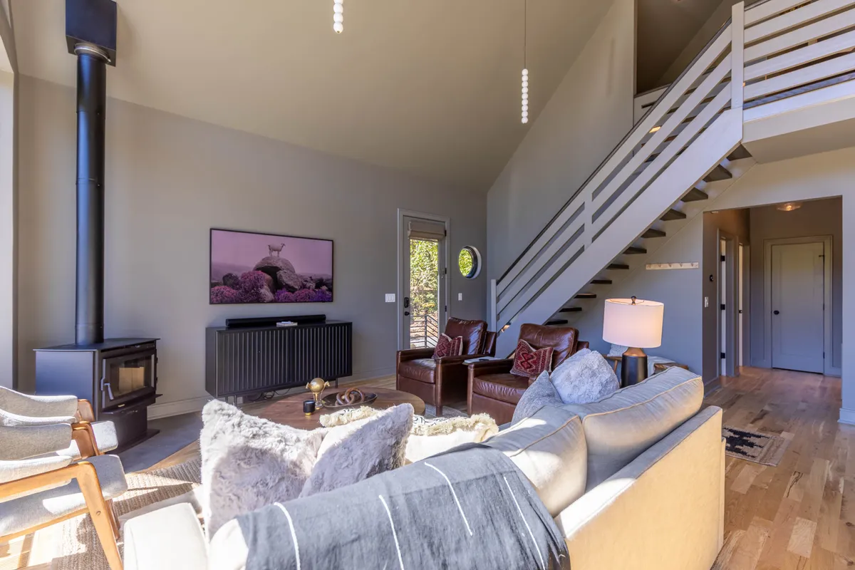 A cozy living room centered around a wood stove, with leather chairs and a plush sofa arranged for conversation. Framed artwork and warm lighting create an inviting, communal atmosphere ideal for socializing and storytelling after a day out.