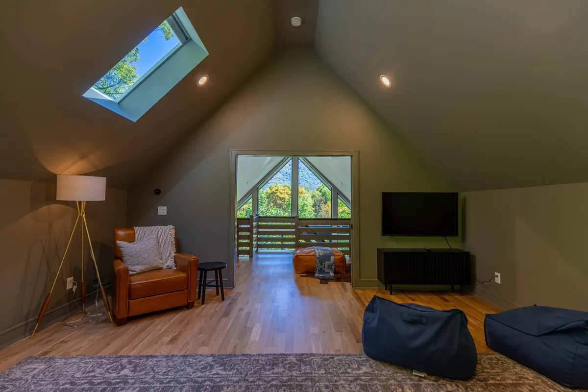 A comfortable sitting area with a skylight, armchair, TV, and a window with sweeping mountain views. Natural light floods the space, emphasizing the connection to the outdoors and the serene setting.