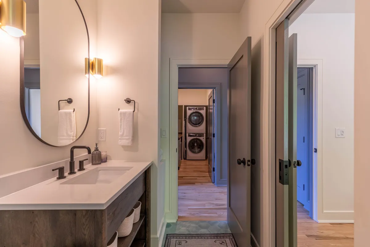 A clean, organized vanity area with a modern sink, large mirror, and a view into a laundry area in the background. The space is bright and practical, balancing beauty and functionality.