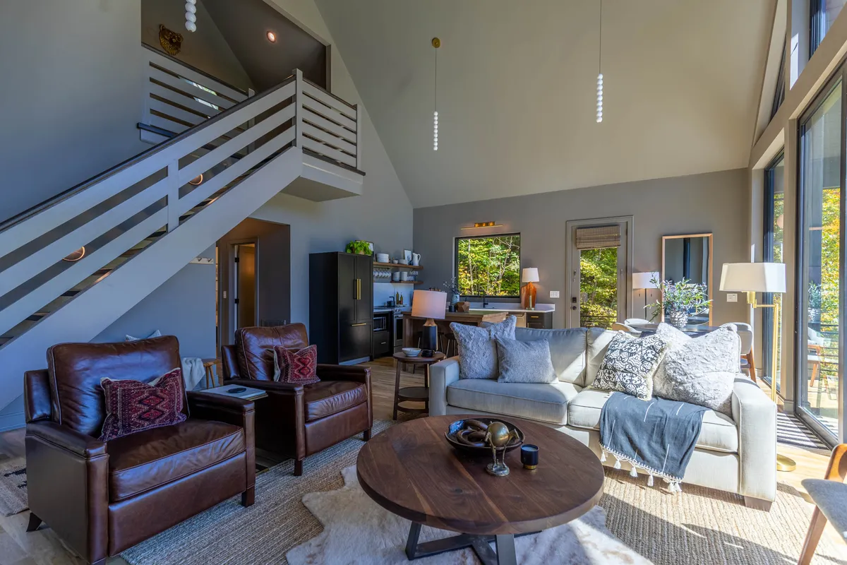 A cozy entryway and seating area with large windows looking onto the outdoors. The decorative staircase and stylish furnishings suggest a thoughtful, flexible design. The entry is welcoming for both guests and their pets after outdoor adventures.