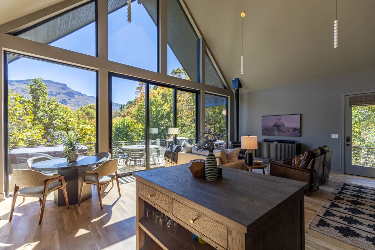 A dining space featuring a large table surrounded by comfortable seating, all oriented towards expansive windows with mountain views. The area is perfect for shared meals and celebrations, enhanced by natural light and a cozy ambiance.