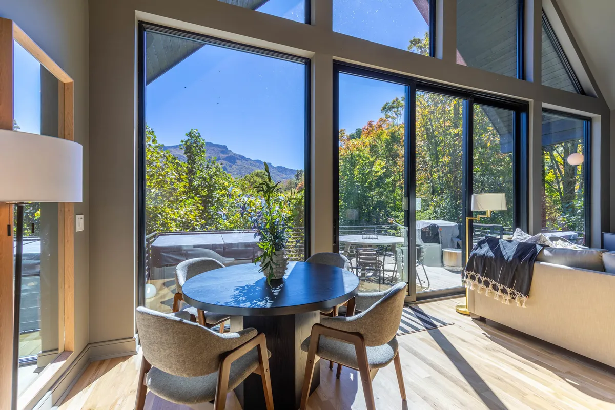 A welcoming space with a round dining table, comfortable seating, and large windows that frame tranquil mountain and nature views. The room invites gatherings and relaxation while keeping the outdoors in sight.