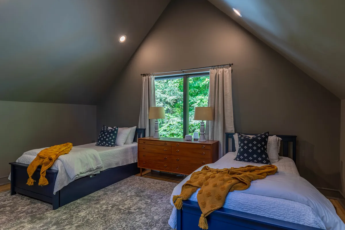 A cozy interior kids’ loft featuring two twin beds, a wooden dresser, and a large window with a scenic view. The inviting decor suggests a comfortable hideaway for younger guests to play, read, or rest after exploring.